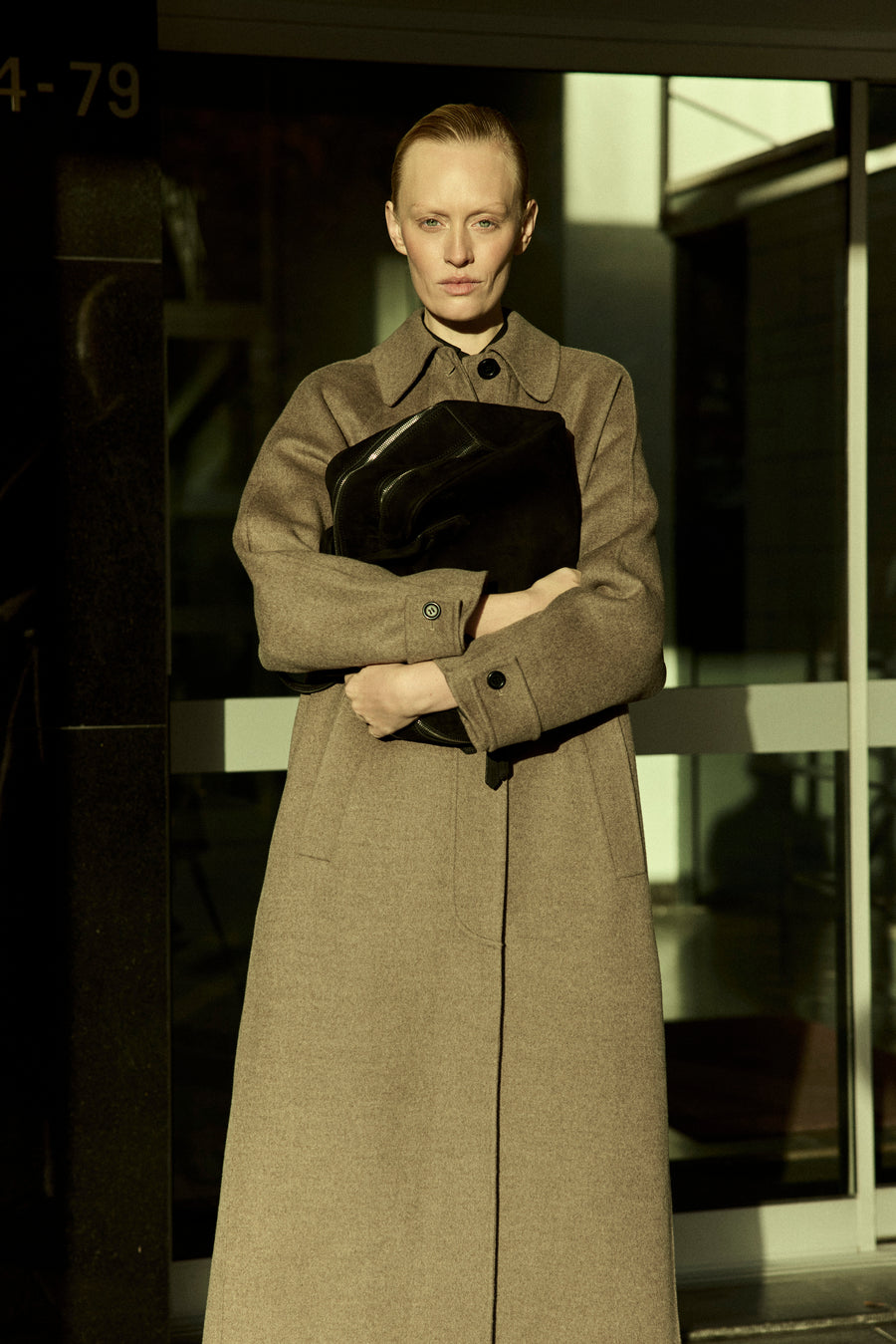 Luca wears the Daniels Coat in Cafe with the Talbot Bag in Black Suede.